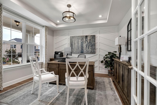 office space with a tray ceiling, a healthy amount of sunlight, a decorative wall, and wood finished floors