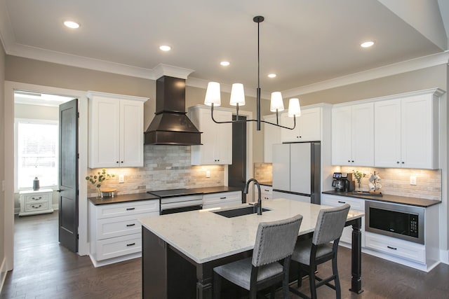 kitchen featuring stainless steel appliances, a sink, dark wood finished floors, a center island with sink, and custom range hood