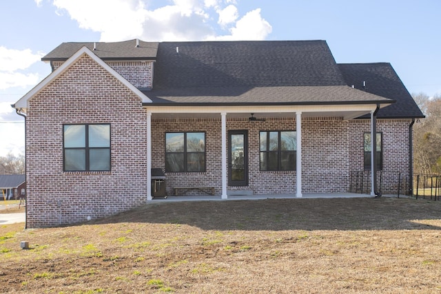 back of house with brick siding, a lawn, and a shingled roof