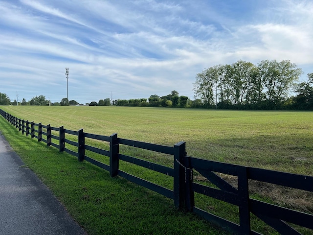 view of gate with a yard, fence, and a rural view