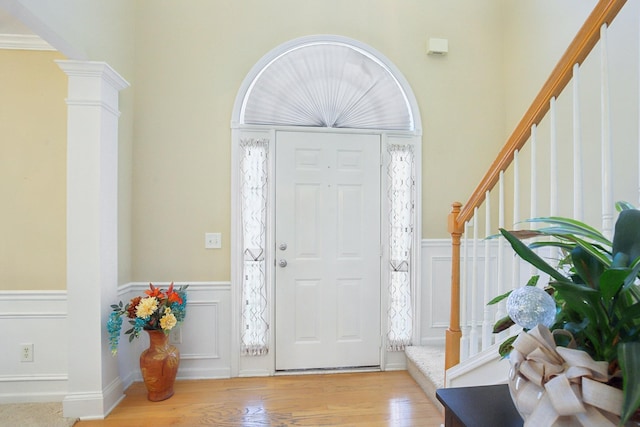 foyer with a decorative wall, a wainscoted wall, wood finished floors, stairway, and ornate columns