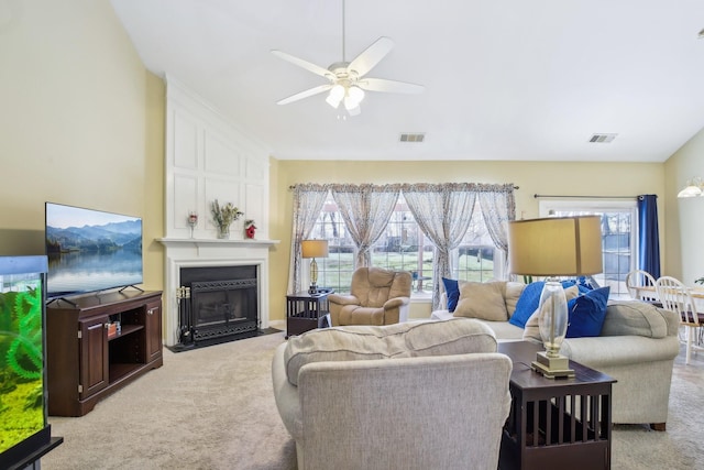 living room with a large fireplace, visible vents, a ceiling fan, and light colored carpet