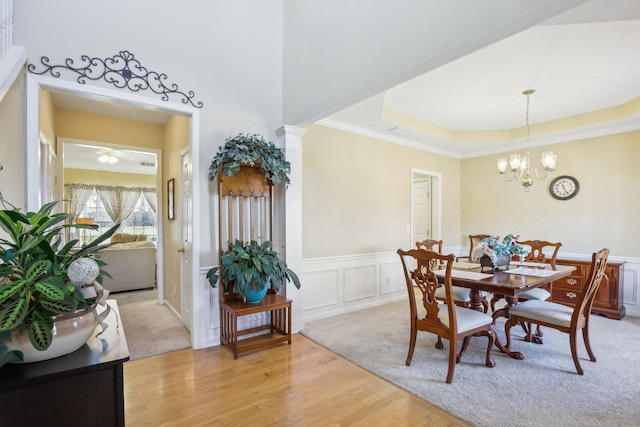 dining space featuring light wood-style floors, a raised ceiling, wainscoting, and a decorative wall