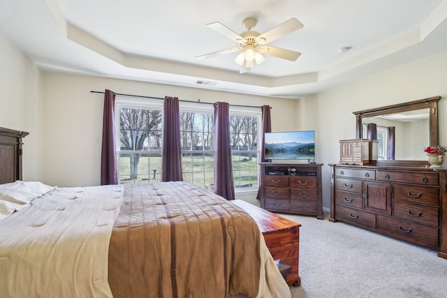 bedroom featuring light carpet, ceiling fan, visible vents, and a raised ceiling