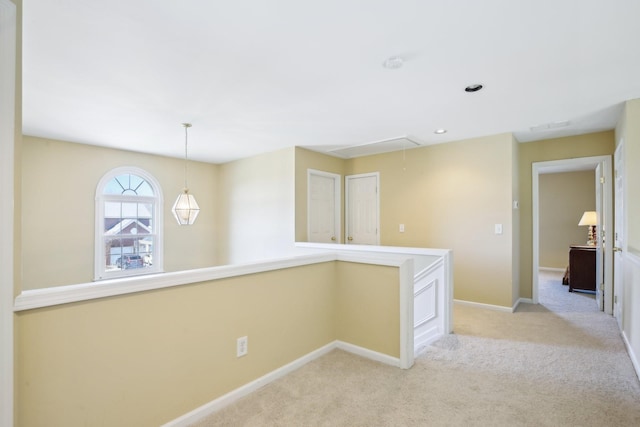 corridor with attic access, baseboards, light carpet, and an upstairs landing