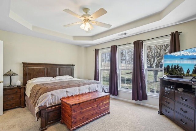 bedroom featuring light carpet, multiple windows, baseboards, and a raised ceiling