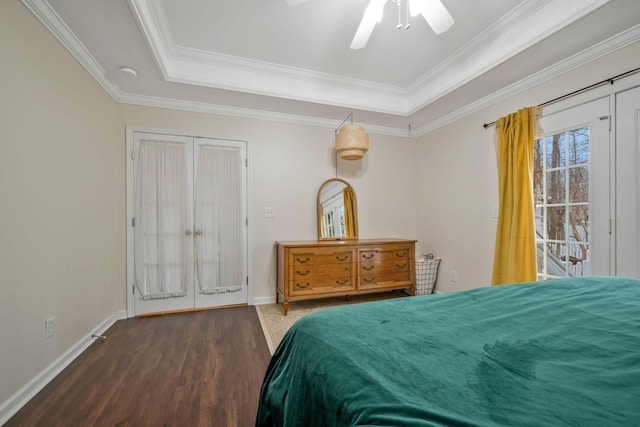 bedroom with ornamental molding, a tray ceiling, baseboards, and wood finished floors