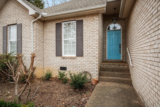 entrance to property featuring crawl space, brick siding, and roof with shingles