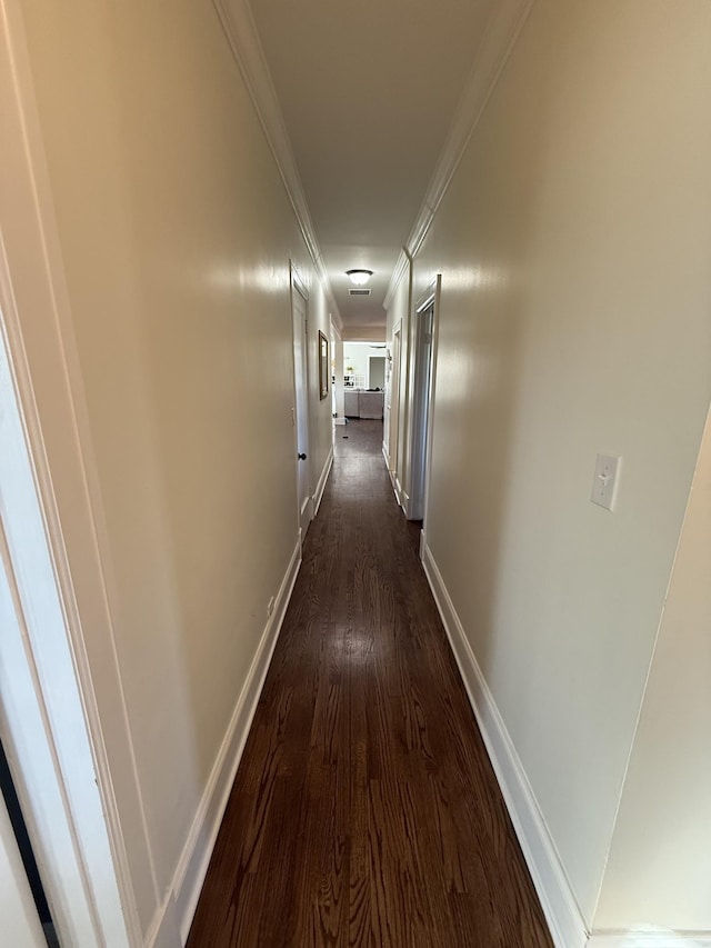 hallway featuring dark wood-style floors, ornamental molding, and baseboards