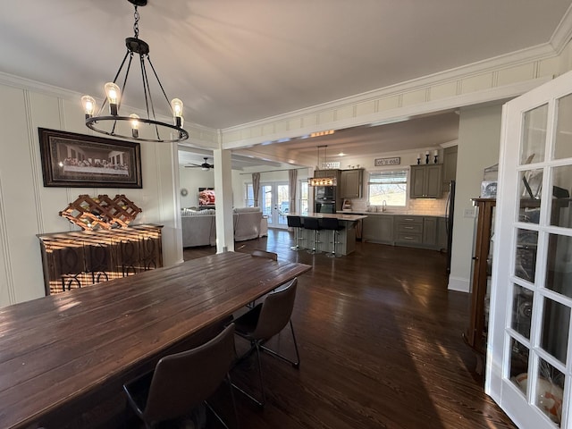 dining area with ornamental molding, french doors, dark wood finished floors, and ceiling fan with notable chandelier