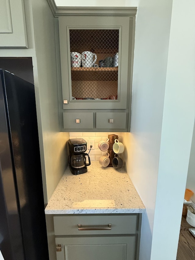 room details featuring tasteful backsplash, light stone counters, freestanding refrigerator, and gray cabinetry