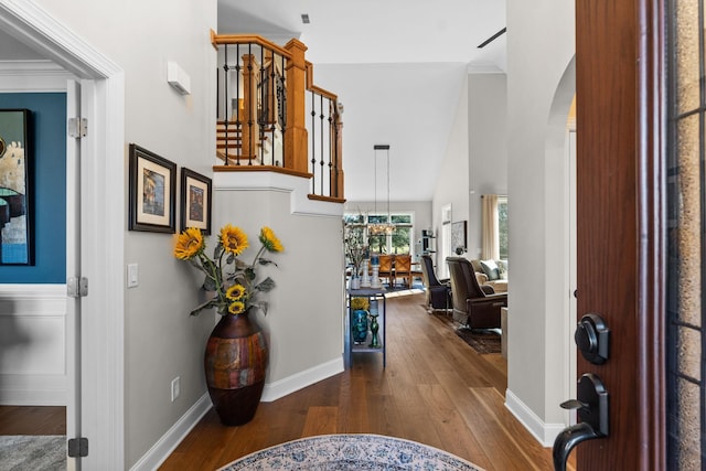 entrance foyer featuring arched walkways, crown molding, a high ceiling, baseboards, and hardwood / wood-style flooring