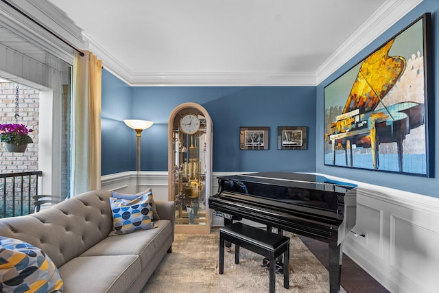 living area with wainscoting, crown molding, a decorative wall, and wood finished floors