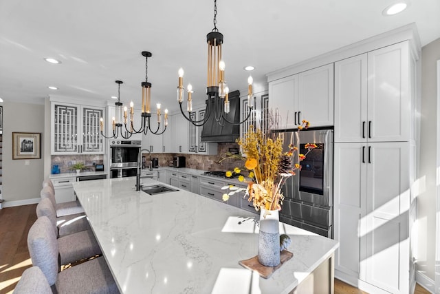 kitchen featuring glass insert cabinets, a sink, custom exhaust hood, stainless steel appliances, and backsplash