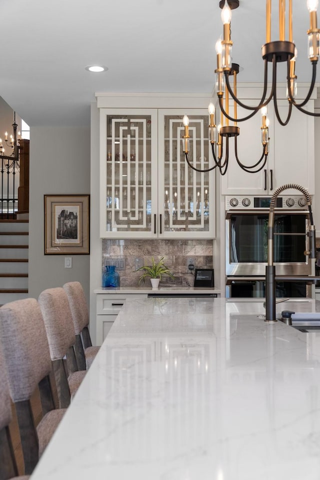 interior space featuring a chandelier, double oven, stairs, backsplash, and decorative light fixtures