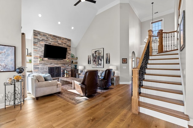 living area featuring high vaulted ceiling, a stone fireplace, stairway, hardwood / wood-style floors, and crown molding