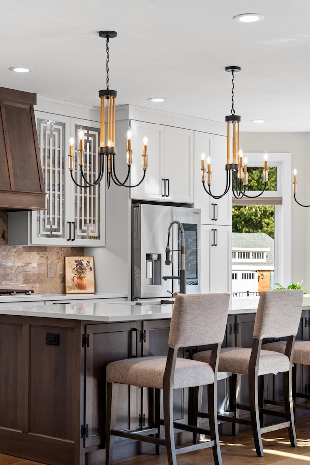 kitchen with dark brown cabinetry, stainless steel fridge with ice dispenser, custom range hood, light countertops, and a chandelier