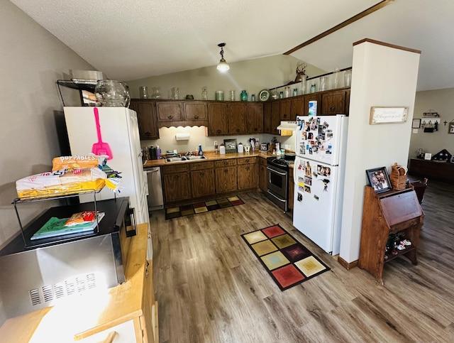 kitchen featuring appliances with stainless steel finishes, lofted ceiling, a sink, and light wood finished floors