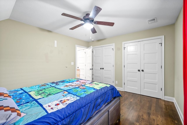 bedroom with baseboards, visible vents, ceiling fan, dark wood-style flooring, and two closets