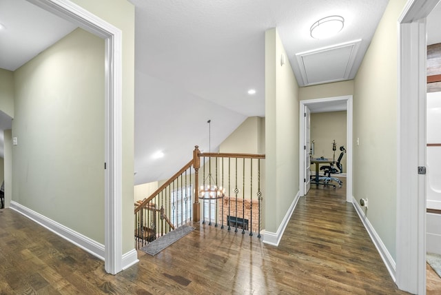 corridor featuring attic access, baseboards, lofted ceiling, wood finished floors, and an upstairs landing