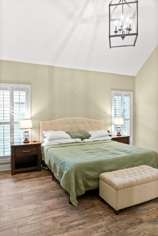 bedroom with a notable chandelier, vaulted ceiling, and wood finished floors