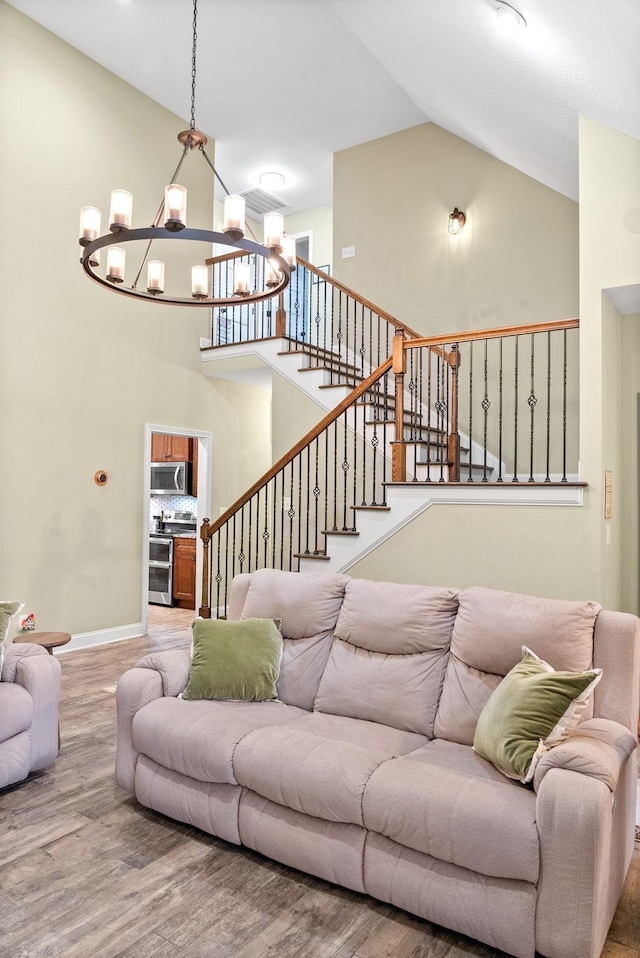 living room with a chandelier, wood finished floors, high vaulted ceiling, baseboards, and stairs