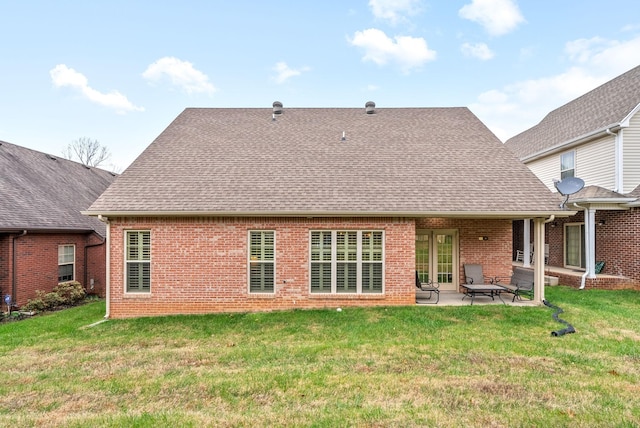 rear view of property featuring brick siding, a shingled roof, a lawn, and a patio