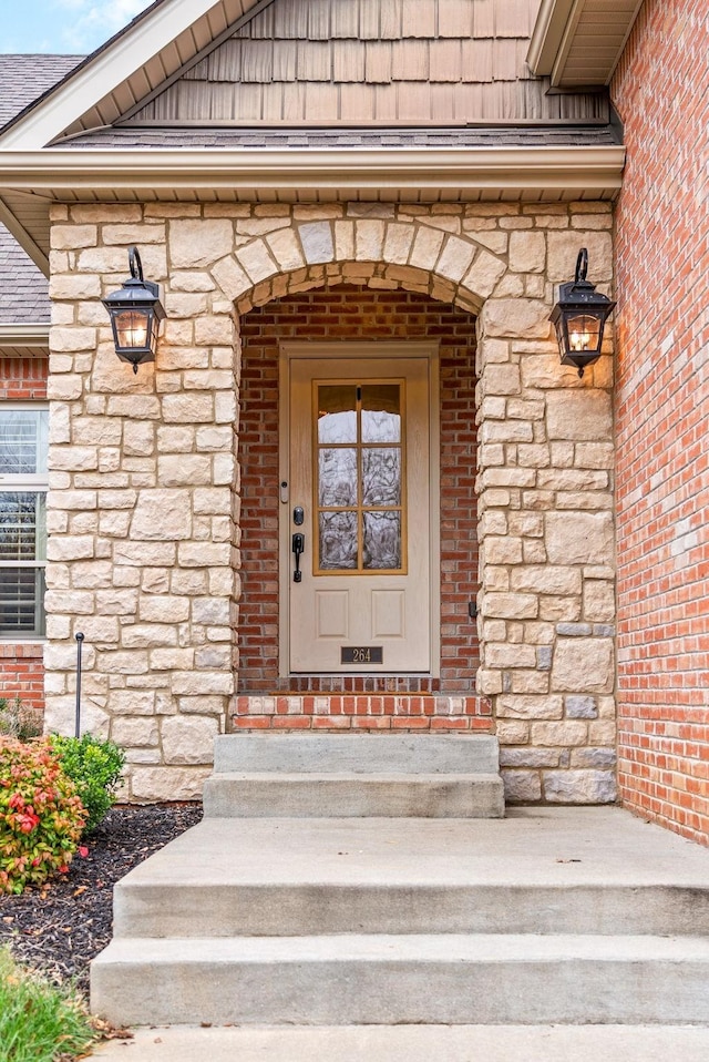 property entrance with a shingled roof, stone siding, and brick siding