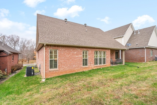 rear view of house featuring roof with shingles, a lawn, brick siding, and central air condition unit