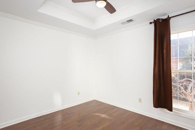 spare room with baseboards, visible vents, ornamental molding, dark wood-type flooring, and a tray ceiling