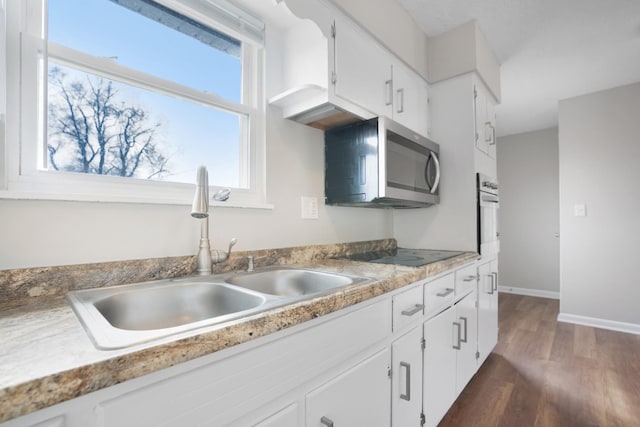 kitchen with black electric cooktop, dark wood-type flooring, a sink, white cabinets, and stainless steel microwave