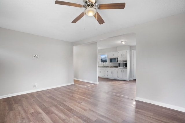 unfurnished living room with ceiling fan, baseboards, and wood finished floors