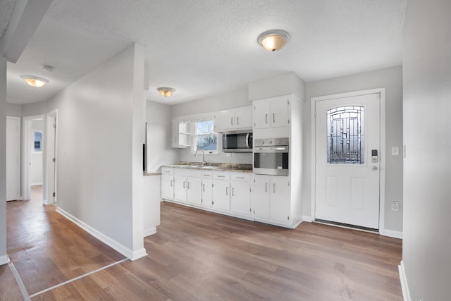 kitchen with a textured ceiling, stainless steel appliances, wood finished floors, baseboards, and white cabinets