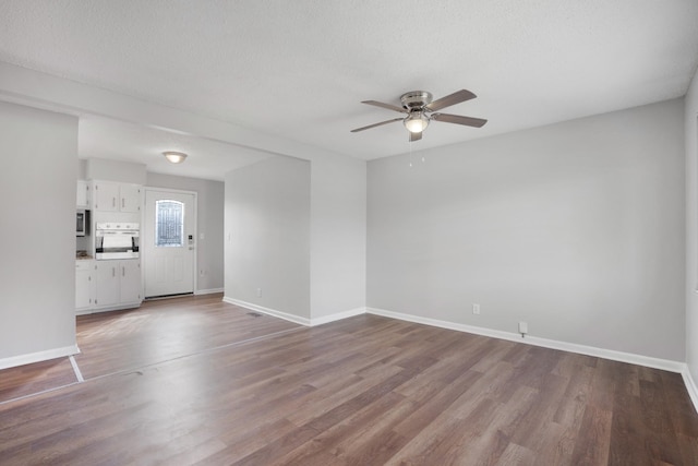 empty room with ceiling fan, a textured ceiling, baseboards, and wood finished floors