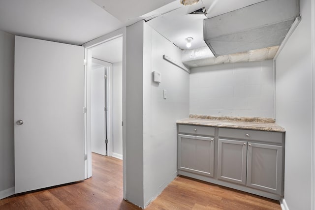 kitchen with light wood-type flooring, baseboards, gray cabinets, and concrete block wall