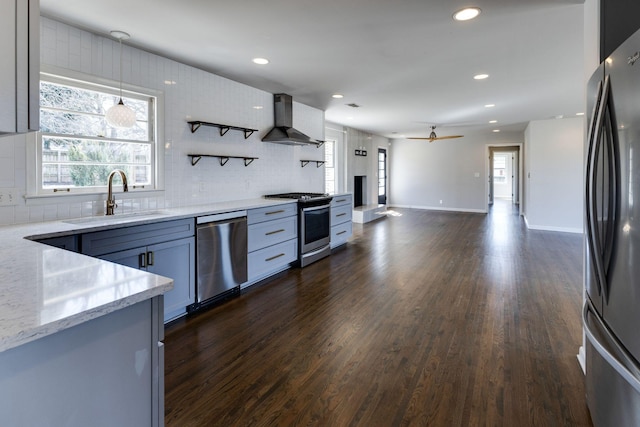 kitchen featuring dark wood-style flooring, a sink, appliances with stainless steel finishes, wall chimney exhaust hood, and tasteful backsplash