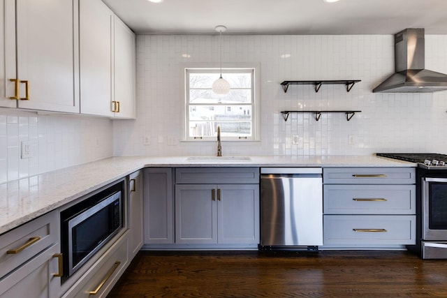 kitchen featuring light stone counters, dark wood-style flooring, appliances with stainless steel finishes, a sink, and wall chimney exhaust hood