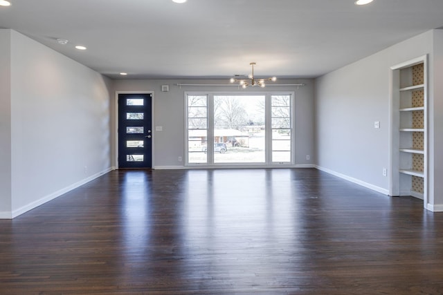 empty room featuring dark wood-style floors, built in shelves, a notable chandelier, recessed lighting, and baseboards