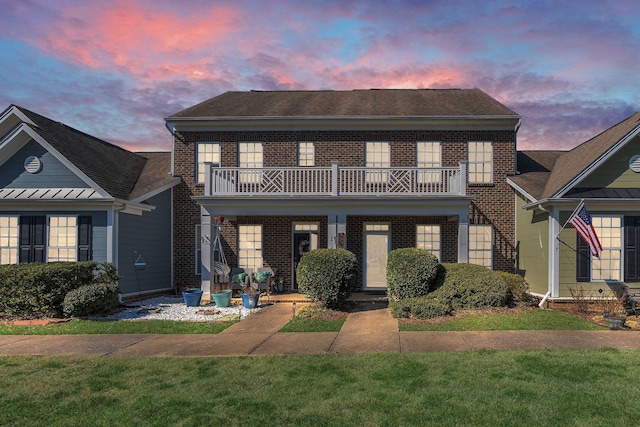 view of front of home featuring brick siding, a front lawn, and a balcony