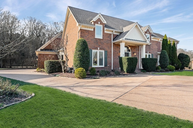 view of front of home with a shingled roof, brick siding, and a front lawn