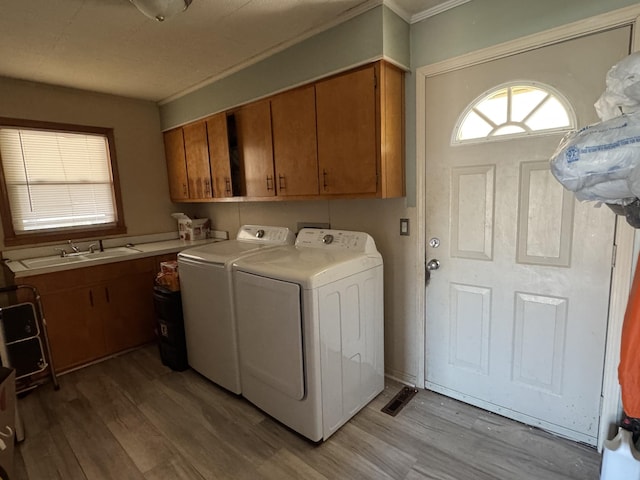 laundry area featuring cabinet space, light wood-style flooring, washer and clothes dryer, and a sink