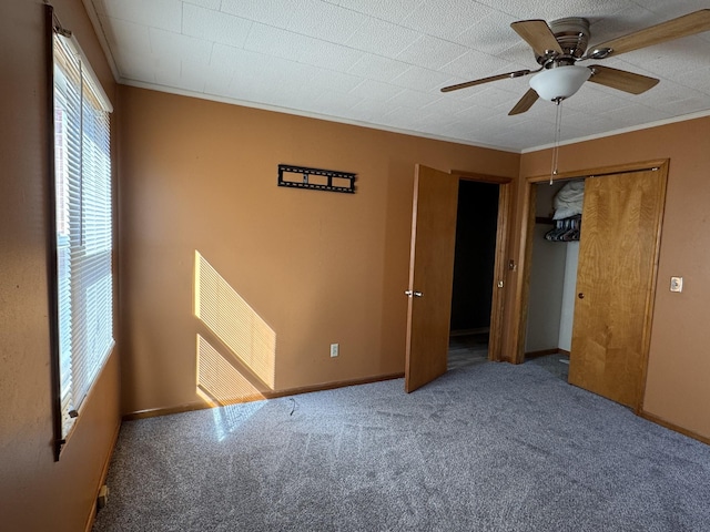 unfurnished bedroom with a closet, ornamental molding, carpet flooring, ceiling fan, and baseboards