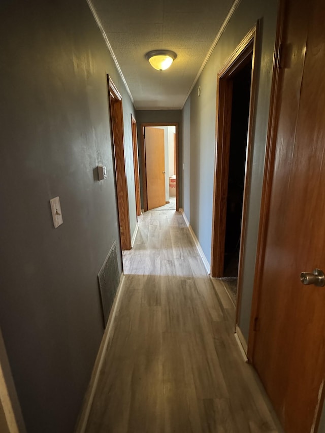 hall with ornamental molding, visible vents, light wood-style flooring, and a textured ceiling