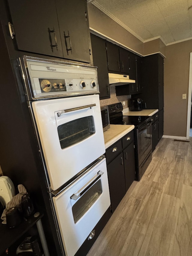 kitchen featuring light wood-type flooring, ornamental molding, dark cabinets, black electric range, and under cabinet range hood