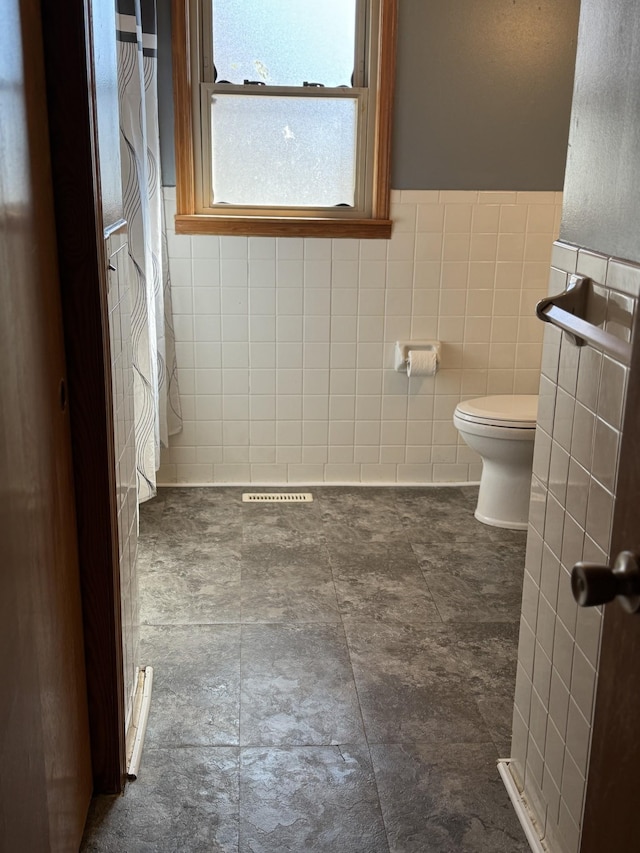 full bathroom with a wainscoted wall, toilet, and tile walls