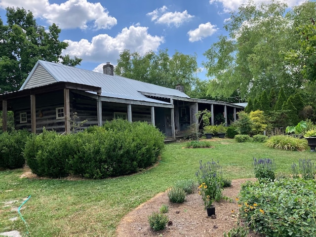 rear view of property with a chimney, metal roof, and a yard