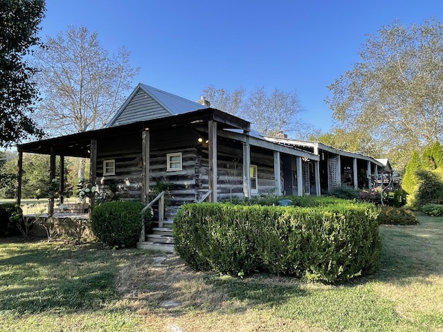 view of front facade with covered porch, a front lawn, log siding, and metal roof