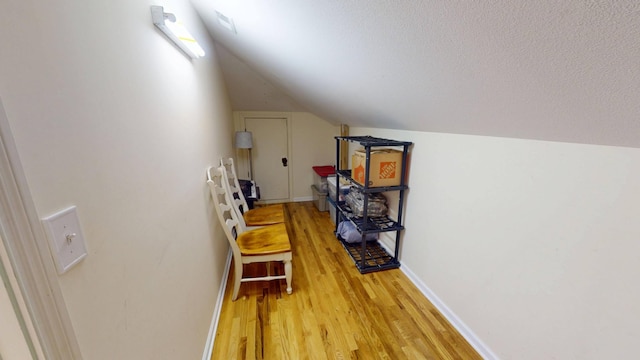 interior space featuring baseboards, light wood-style flooring, a textured ceiling, and lofted ceiling