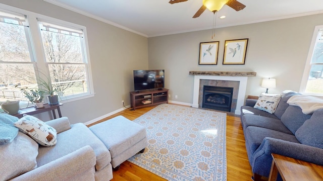 living room featuring a tiled fireplace, wood finished floors, crown molding, baseboards, and ceiling fan