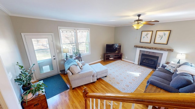 living room featuring a ceiling fan, wood finished floors, baseboards, a fireplace, and ornamental molding